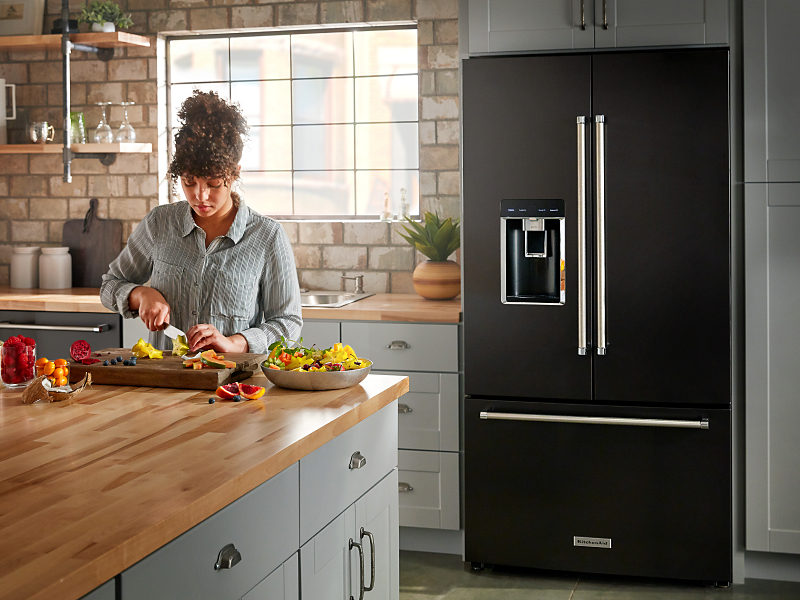 A person making a meal in a modern kitchen next to a KitchenAid® refrigerator.