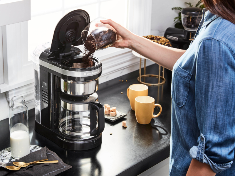 Woman pouring ground coffee into KitchenAid® coffee maker