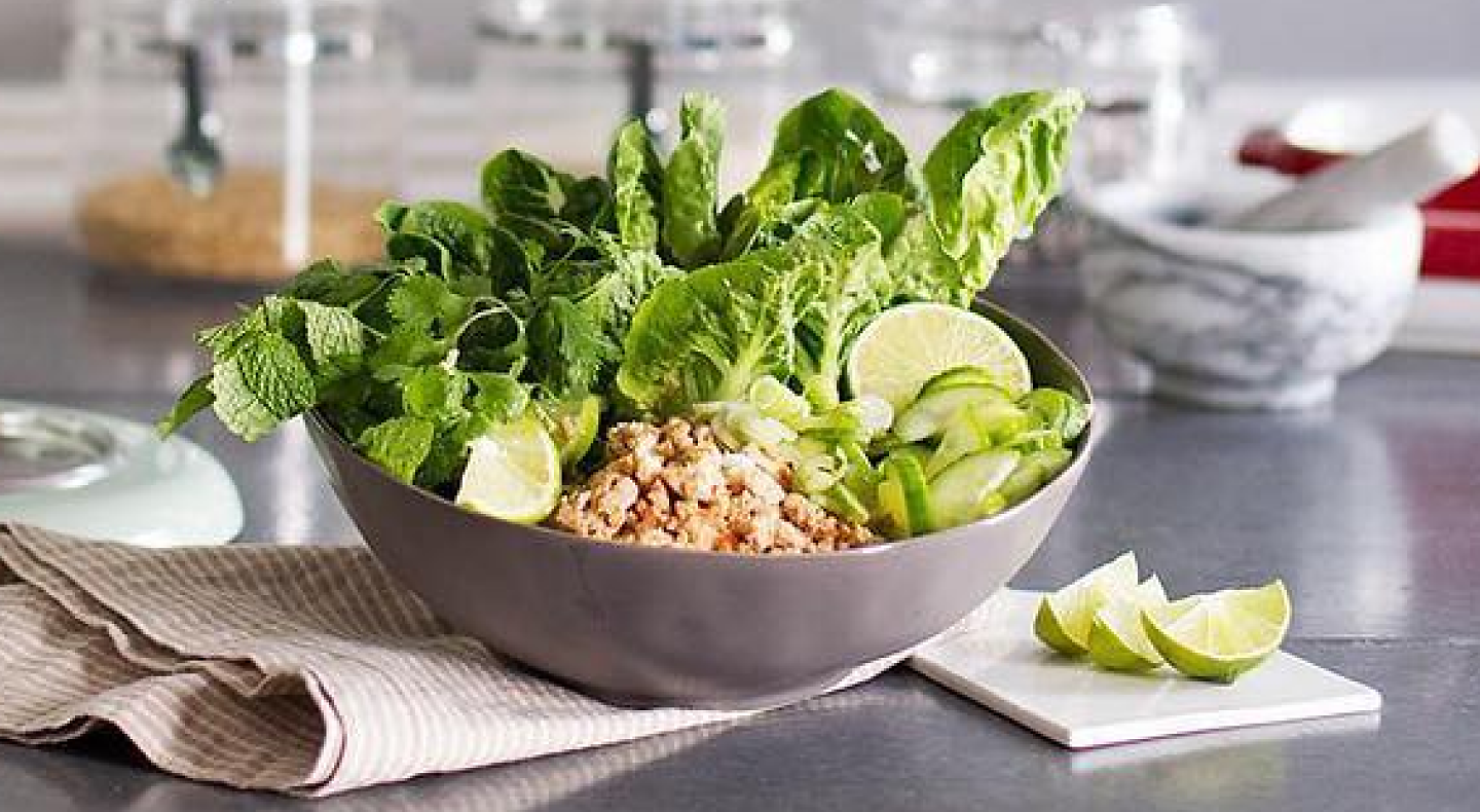 Lettuce salad with lime wedges in gray bowl on countertop