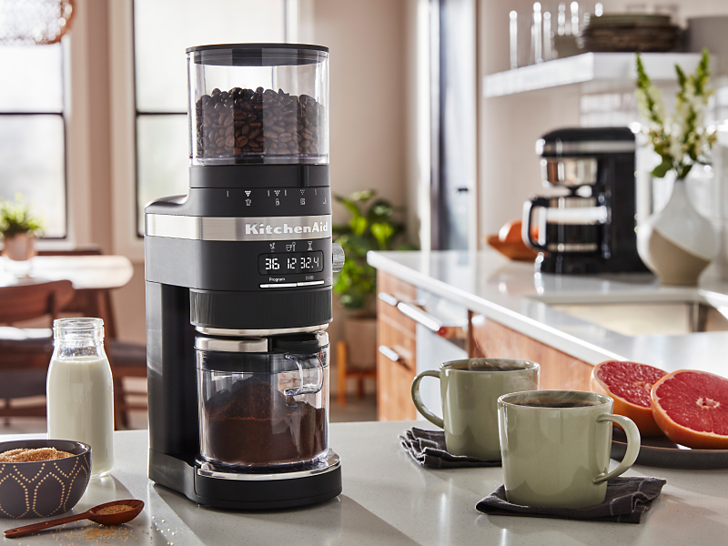 Coffee maker on counter with mugs full of coffee and halved grapefruit pieces 