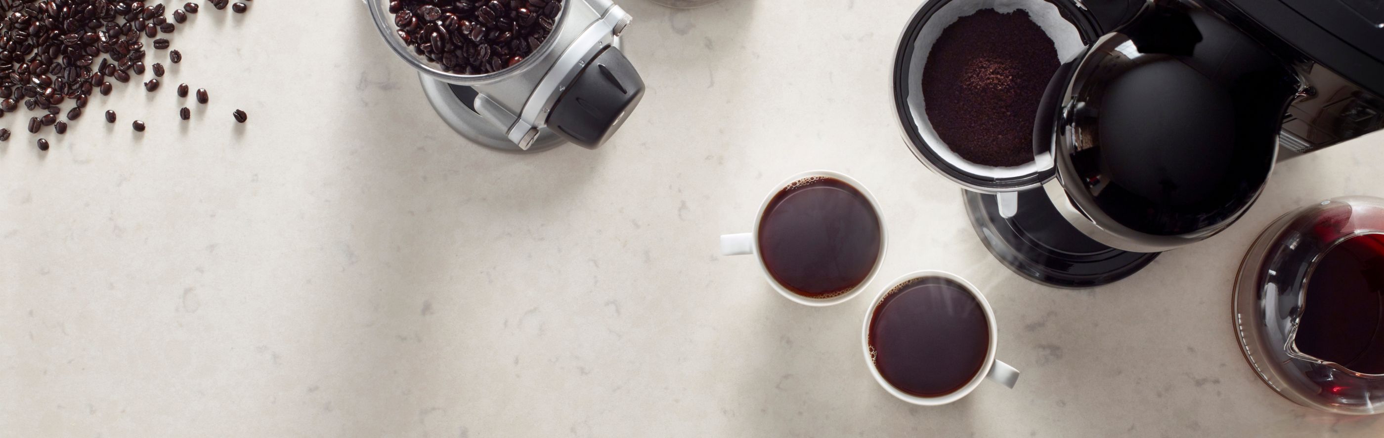 Bird’s-eye view of full cups of coffee, a coffee maker and a coffee grinder near coffee beans