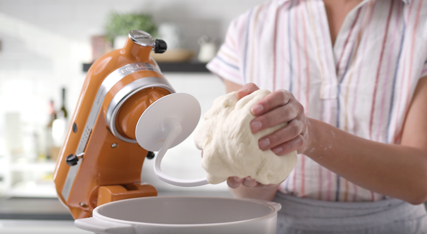 Bread dough being removed from a dough hook attached to an orange tilt-head KitchenAid® stand mixer.