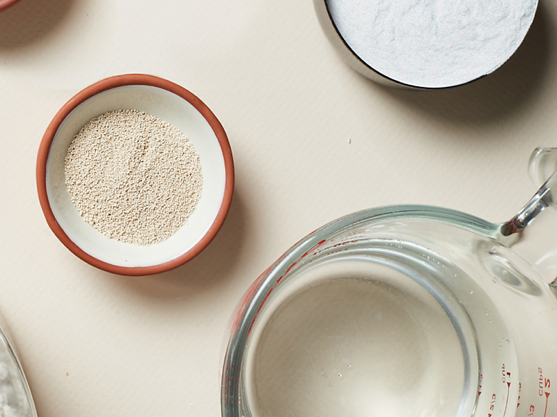 Dry ingredients like yeast and flour in small bowls next to a measuring cup with water