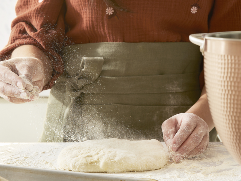 A person lightly flouring risen dough on a work surface