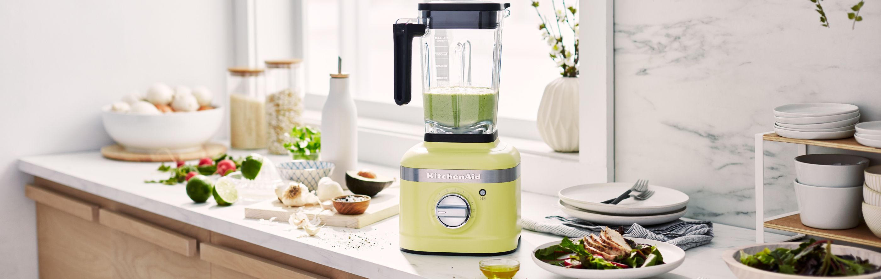 A green KitchenAid® blender with limes and a chicken salad nearby.