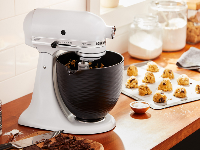 A white KitchenAid® stand mixer next to a sheet of cookie dough 