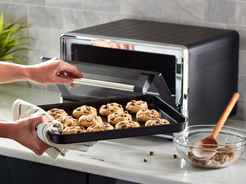 A person placing a sheet with cookie dough into a countertop oven