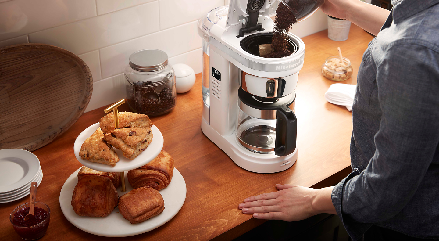 Woman pouring coffee grounds into drip coffee maker