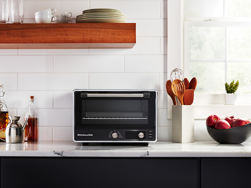 A KitchenAid® countertop oven with marinades and apples nearby.