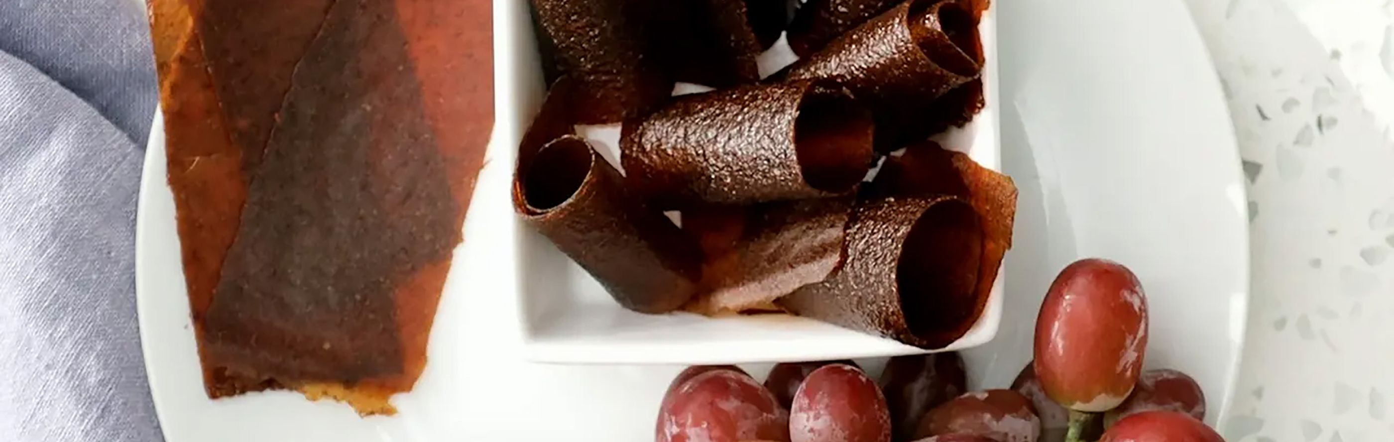 Homemade fruit leather and grapes on white dishware.
