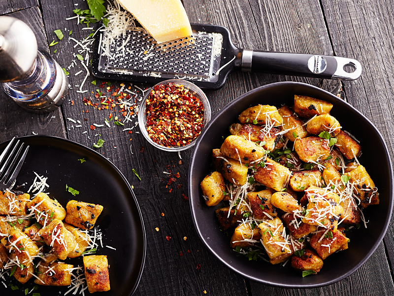 Two bowls of potato gnocchi meals with fresh parmesan, red pepper flakes and herbs. 