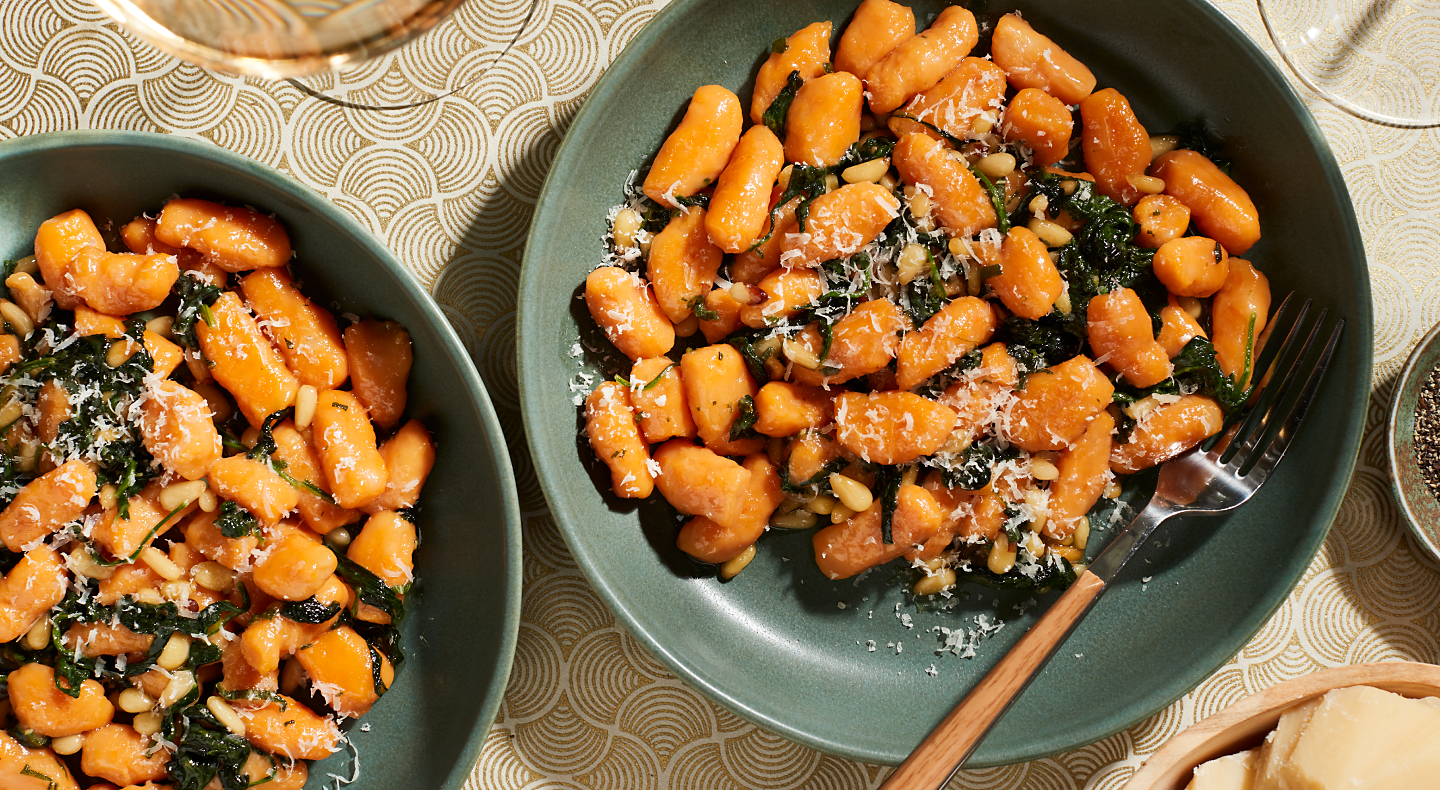 Two bowls of sweet potato gnocchi meals with shaved parmesan, spinach and herbs.