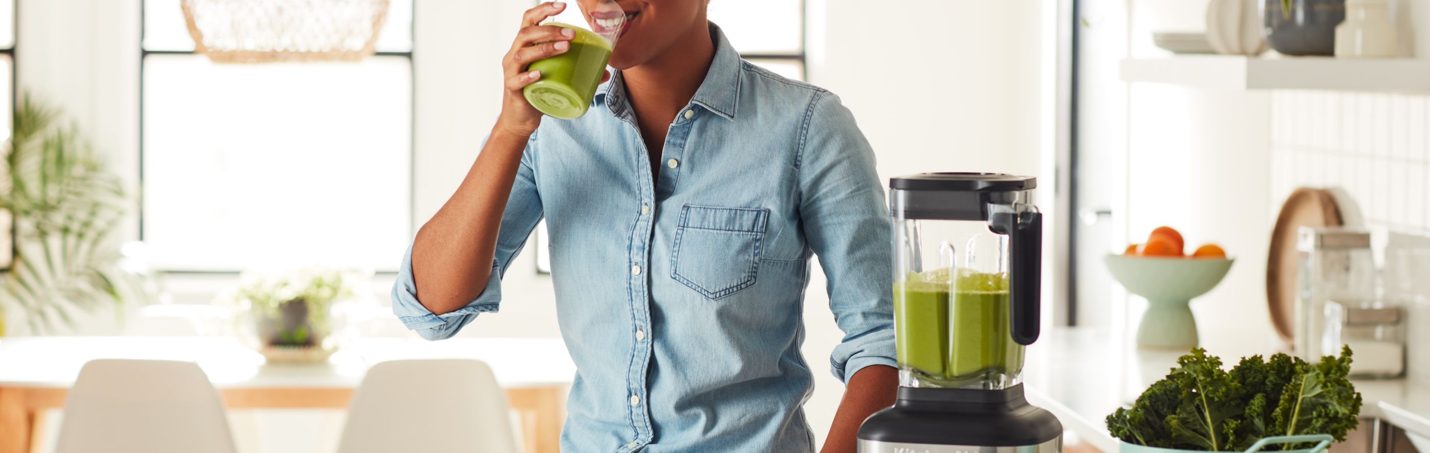 Person drinking green juice next to a KitchenAid® blender