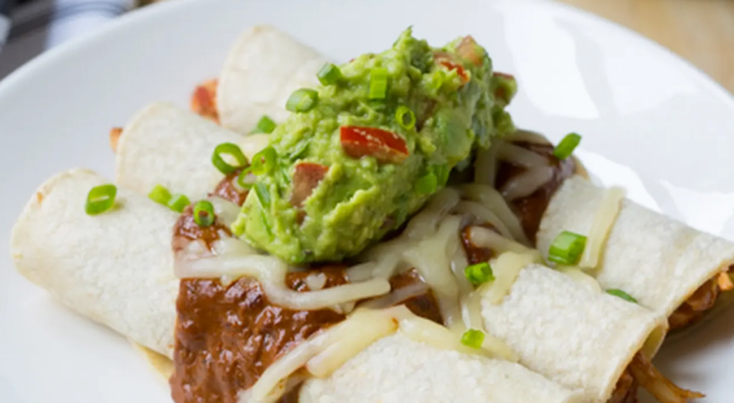 A plate of enchiladas topped with guacamole. 
