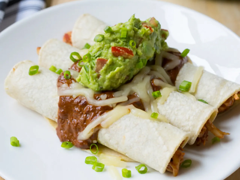 A plate of enchiladas topped with guacamole. 