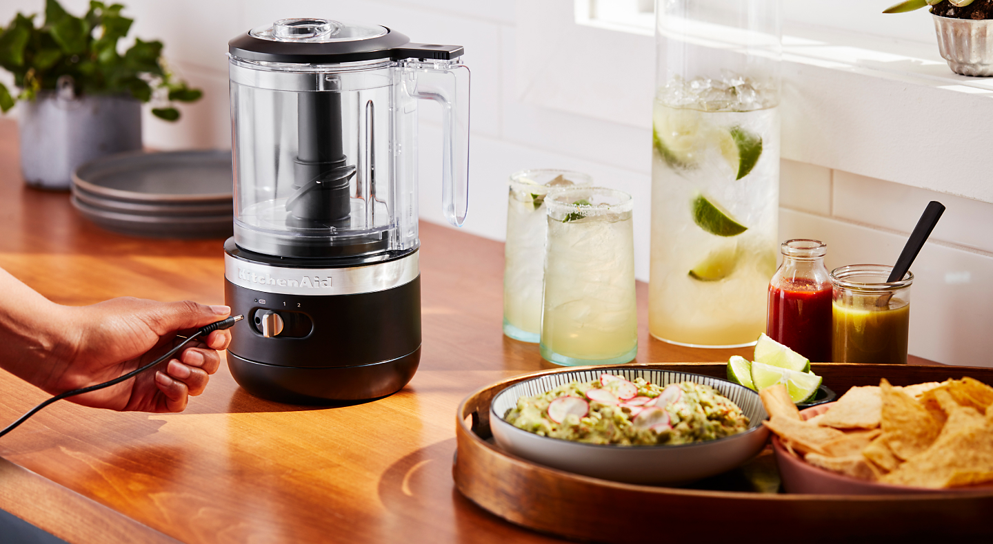 A cordless KitchenAid® food chopper next to a platter of guacamole and tortilla chips and a pitcher and glasses of margaritas. A cordless KitchenAid® food chopper next to a platter of guacamole and tortilla chips and a pitcher and glasses of margaritas. 