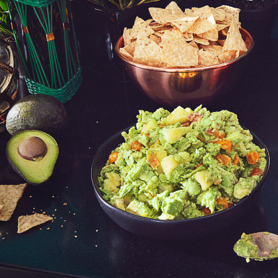 A bowl of fresh guacamole next to a bowl of tortilla chips.