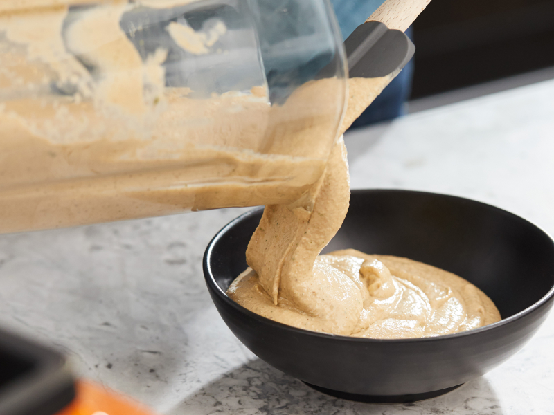 Puréed dip being removed from blender jar with a gray rubber spatula