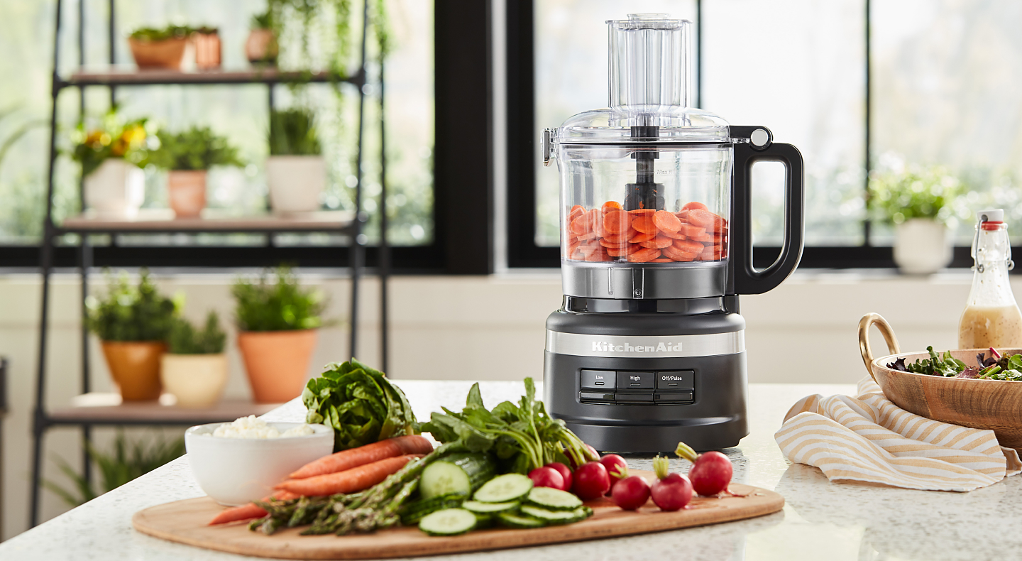 A KitchenAid® food processor mixing vegetables in a bright, modern kitchen.