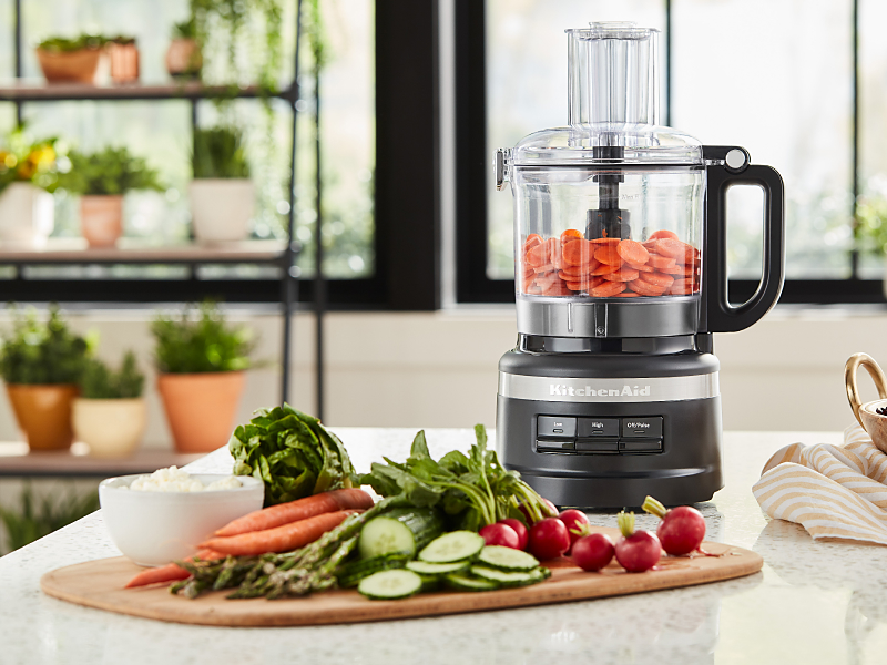 A KitchenAid® food processor mixing vegetables in a bright, modern kitchen.