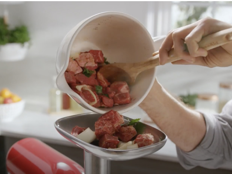 Person adding cubes of meat into a KitchenAid® Meat Grinder Attachment