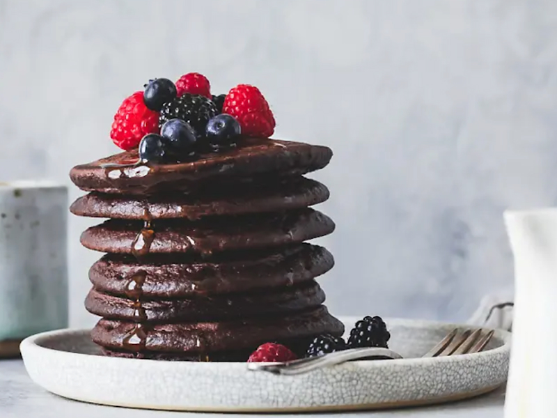 Stack of cocoa pancakes drizzled with syrup and topped with fresh fruit