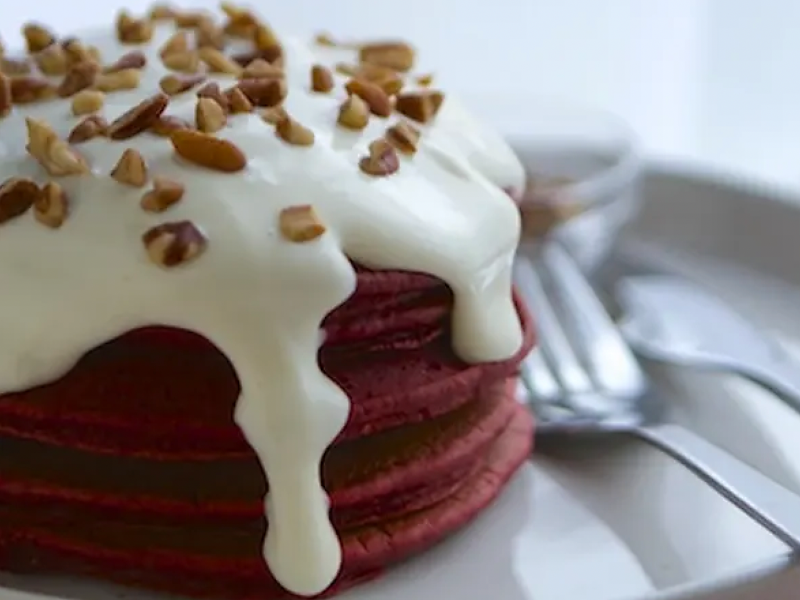 Stack of red velvet pancakes with cream cheese drizzle and nut topping
