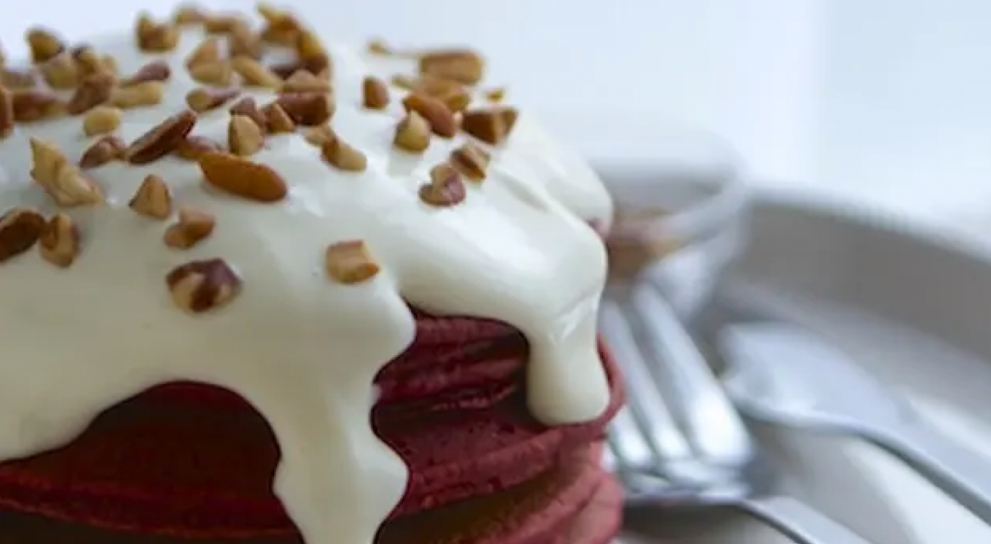 Stack of red velvet pancakes with cream cheese drizzle and nut topping