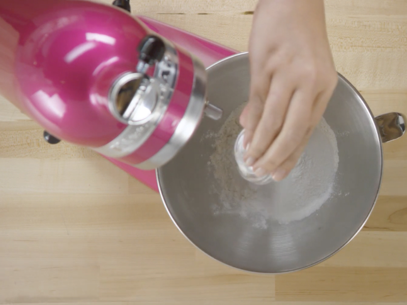 Close-up of person adding ingredients to stand mixer bowl