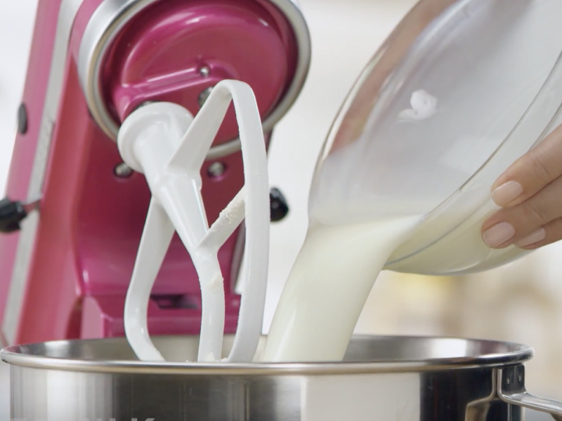 Person pouring milk from mixing bowl into stand mixer bowl