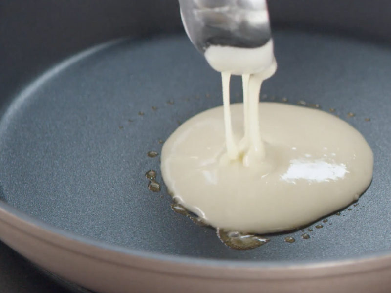 Person pouring pancake batter into prepared skillet