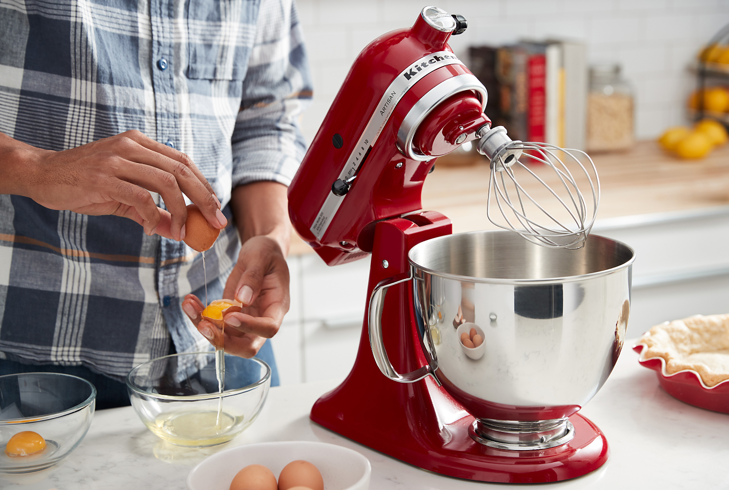Person cracking eggs next to a KitchenAid® stand mixer with wire whip