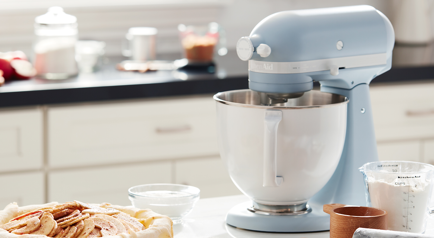 Blue KitchenAid® stand mixer on countertop with baking ingredients and plate of cookies