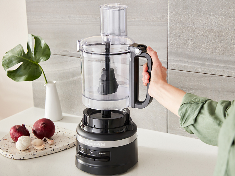 Person placing the work bowl of a black KitchenAid® food processor onto the base