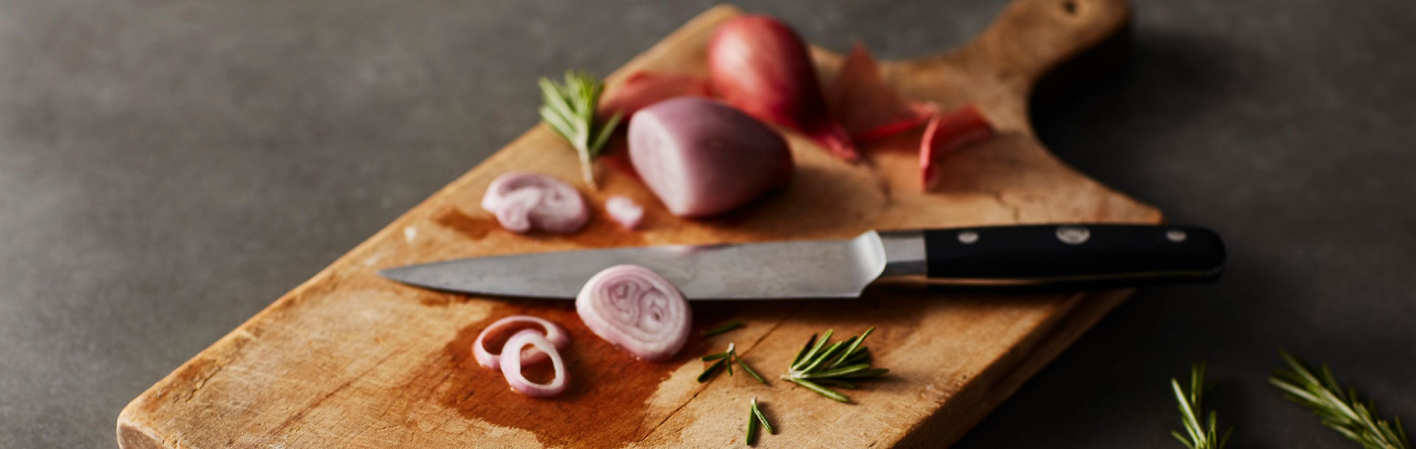 Wooden cutting board with partially cut red onion and knife on top