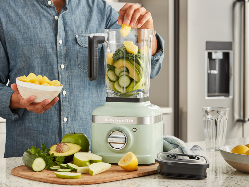 Person adding fruits and vegetables to a blender jar