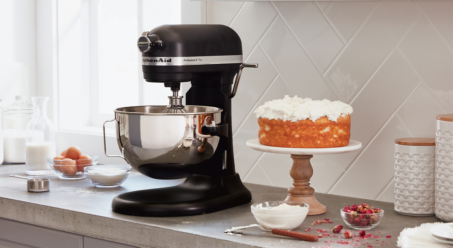 A black KitchenAid® stand mixer next to a cake