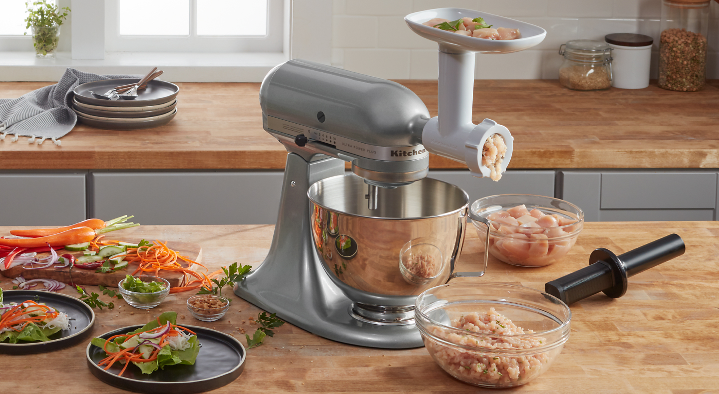KitchenAid® stand mixer with KitchenAid® food grinder attachment and clear bowl of ground chicken