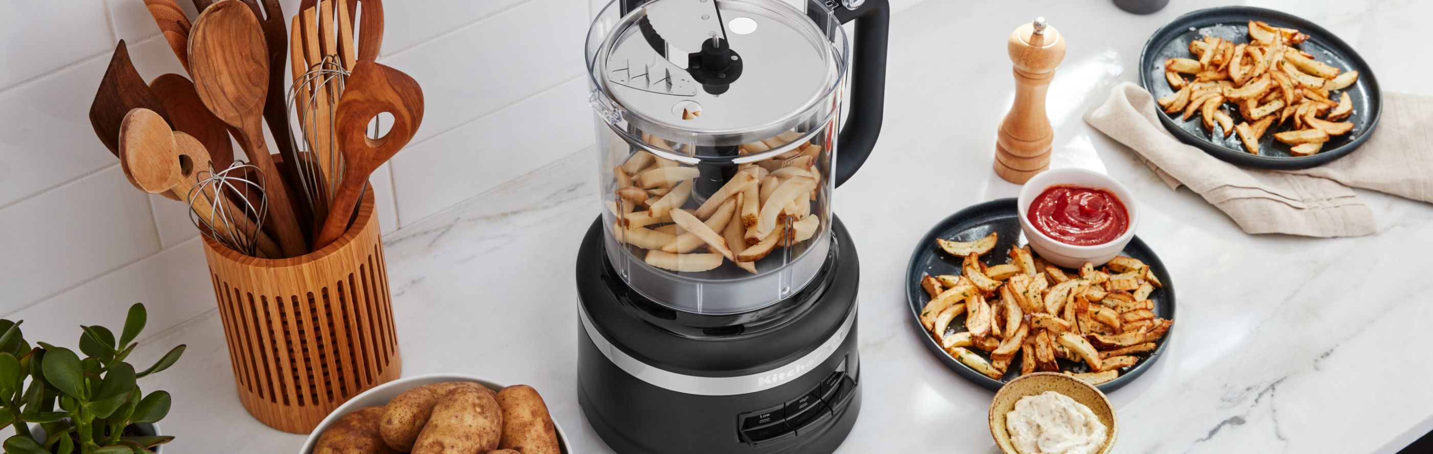KitchenAid® food processor on a modern kitchen counter next to plates of french fries