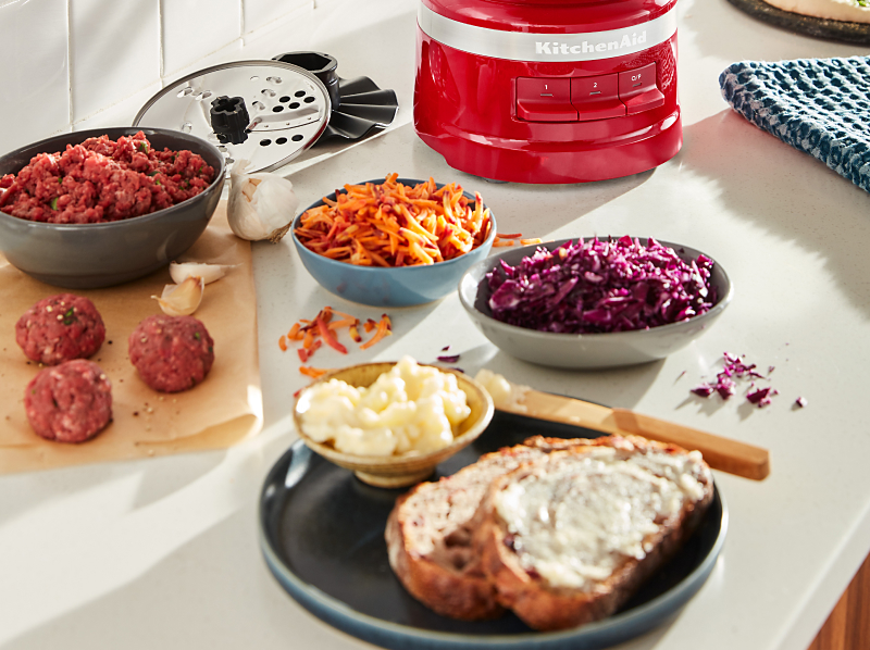 Modern kitchen counter with a bowl of shredded purple cabbage, shredded carrots, garlic cloves, meatballs and a plate of bread with a creamy spread