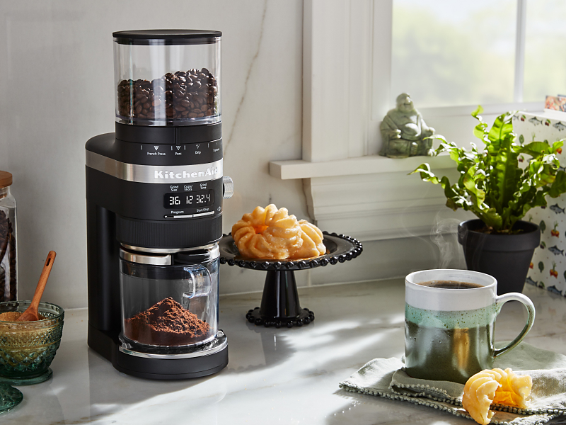 Burr grinder on a counter with pastries and brewed coffee