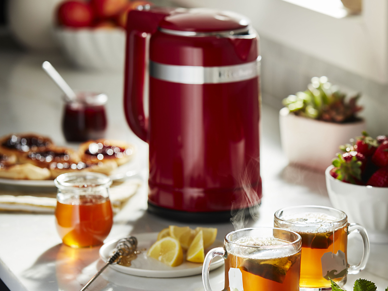 Red KitchenAid® electric kettle on countertop next to glasses of hot tea