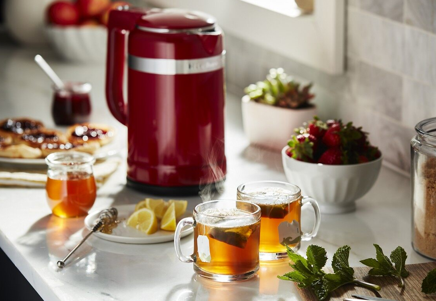 Red electric tea kettle on countertop with tea and food