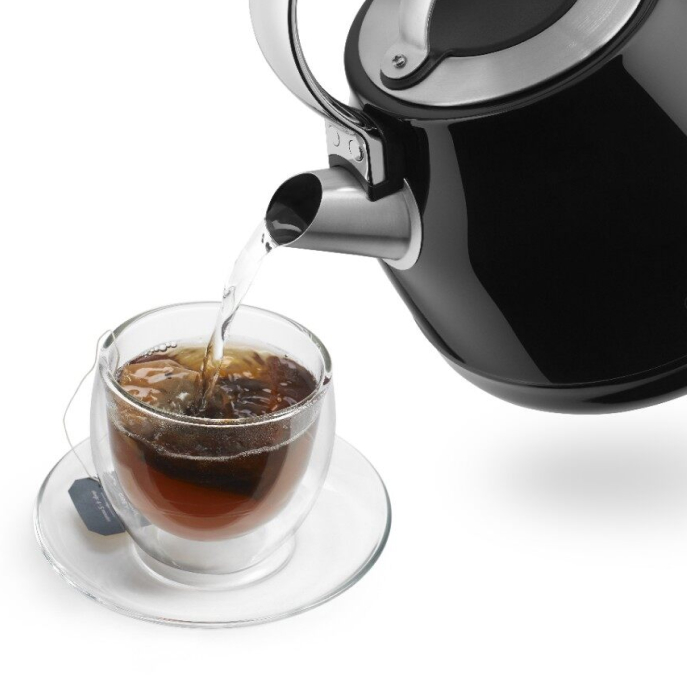 Black electric kettle pouring water over tea bag in glass