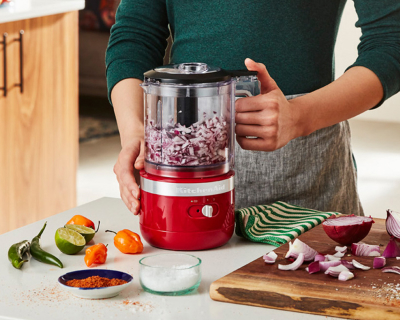 Person pulsing red onions in red food chopper on counter with ingredients
