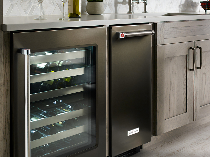 A black KitchenAid® ice maker next to an open wine cooler