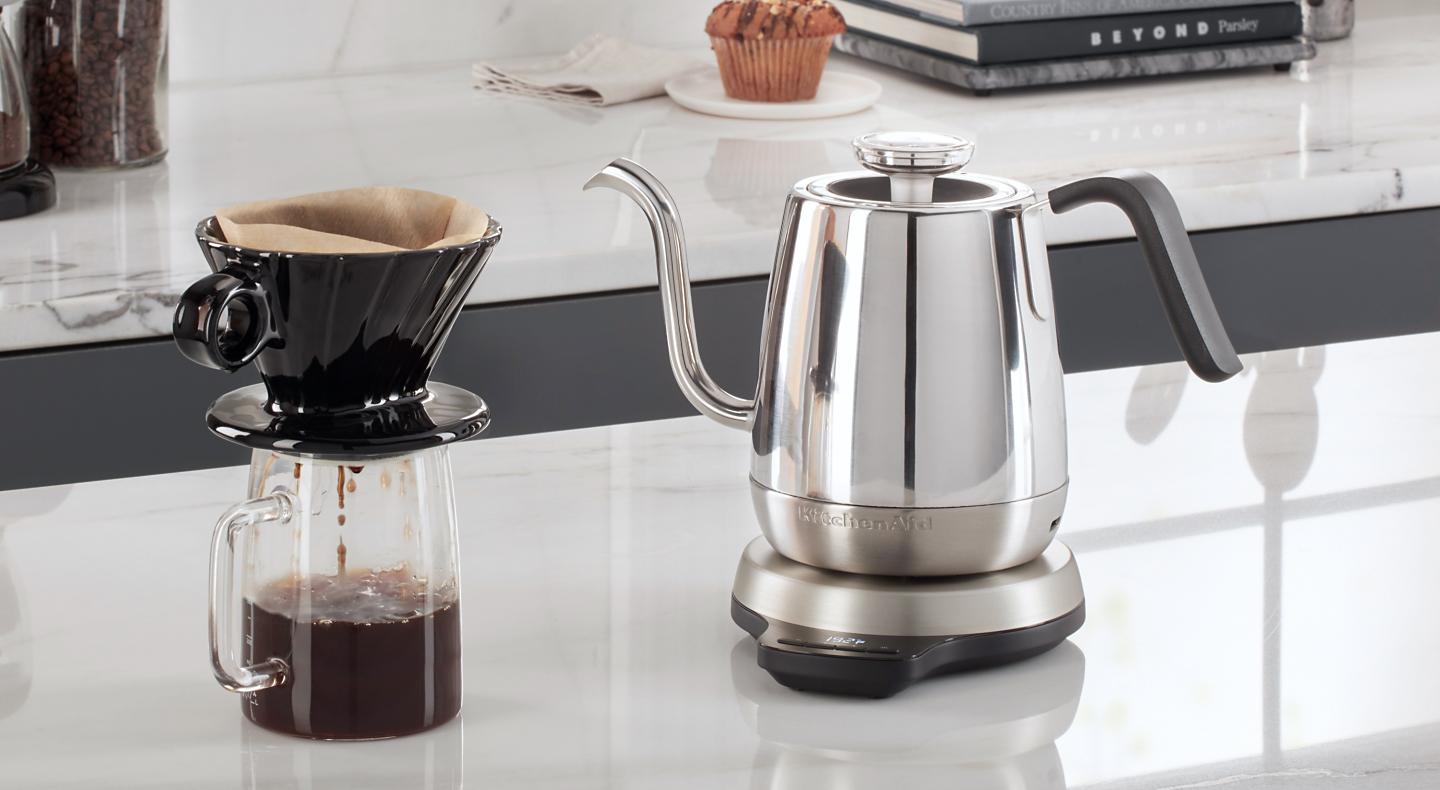 Silver KitchenAid® gooseneck kettle on white countertop with cup of pour over coffee