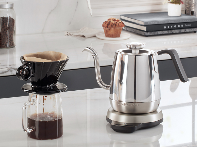 Silver KitchenAid® gooseneck kettle on white countertop with cup of pour over coffee