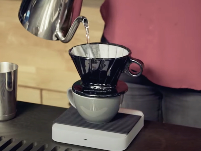Maker pouring boiled water from electric kettle into pour over coffee filter