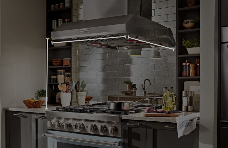 Wall-mount commercial-style KitchenAid® hood above KitchenAid® gas range with animated overlay of height, width and depth markers